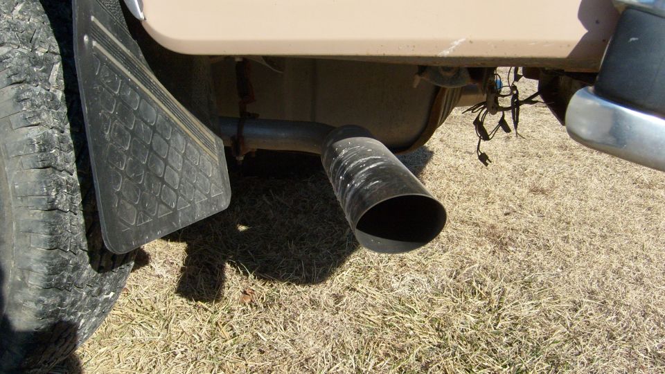 Large angle-cut exhaust tip under tan truck body behind rear tire and mud flap