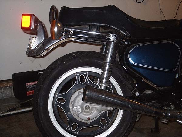 Rear left of a motorcycle with mag wheel, chrome exhaust and blue tank in a garage