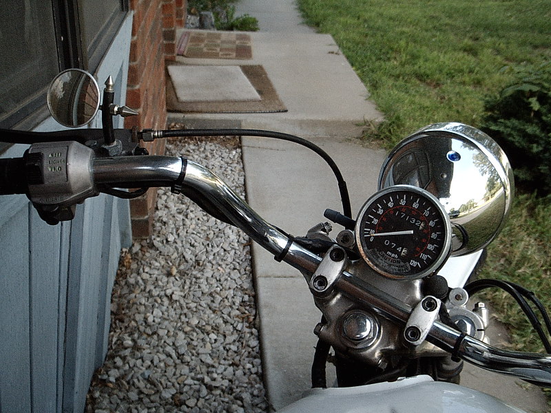 View over a motorcycle's chrome handlebars showing single speedometer and chrome headlight bucket