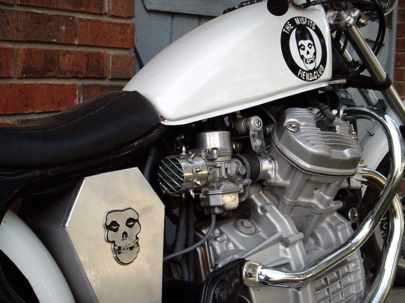 Custom motorcycle with white tank and Misfits skull decals, engine and carb detail