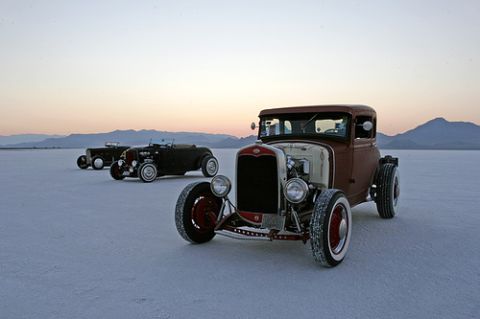 1989 Ford Bronco - Three vintage hot rod cars are lined up on a vast salt flat with mountains in the background.