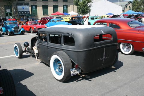 1989 Ford Bronco - A custom hot rod sedan with a matte black finish and distinctive pinstripe art is displayed at an outdoor car show.