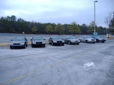 1996 Ford Crown Victoria - A group of Ford Crown Victorias are parked in an outdoor lot under a cloudy sky.