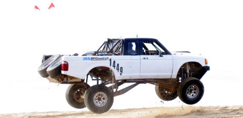 1984 Ford Bronco - Modified Ford Ranger jumps during an off-road event, showing custom suspension and spare tires.