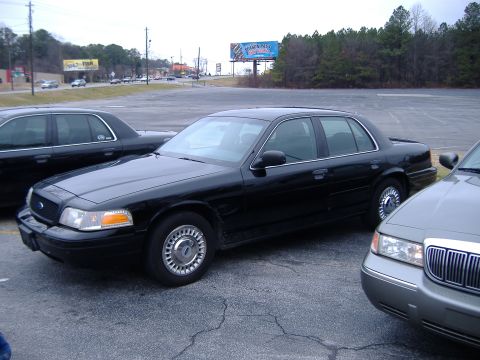 1996 Ford Crown Victoria - Three Ford Crown Victorias are parked in an asphalt lot under an overcast sky.