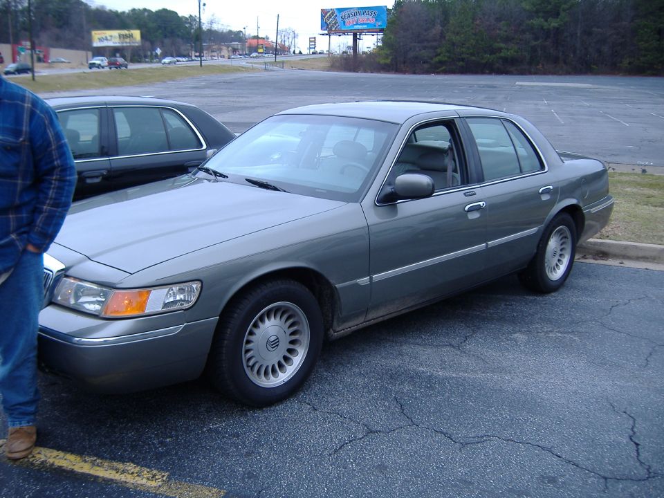 Gray sedan parked in a lot, side view. The car has a chrome trim line along the bottom of the doors and a distinctive wheel design