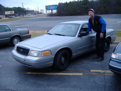 1996 Ford Crown Victoria - A silver 1996 Ford Crown Victoria is parked in a lot, with a man standing next to the driver's side door.