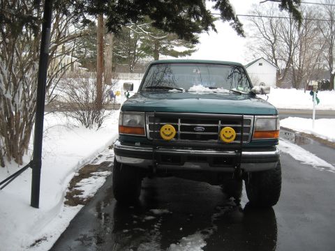 1996 Ford Bronco - A green Ford truck is parked on a wet driveway with snow on the ground and on the vehicle.