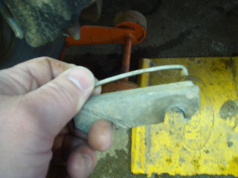1996 Ford Bronco - A hand holds a rusty brake caliper bracket with a metal clip, against a backdrop of yellow and orange mechanical parts.