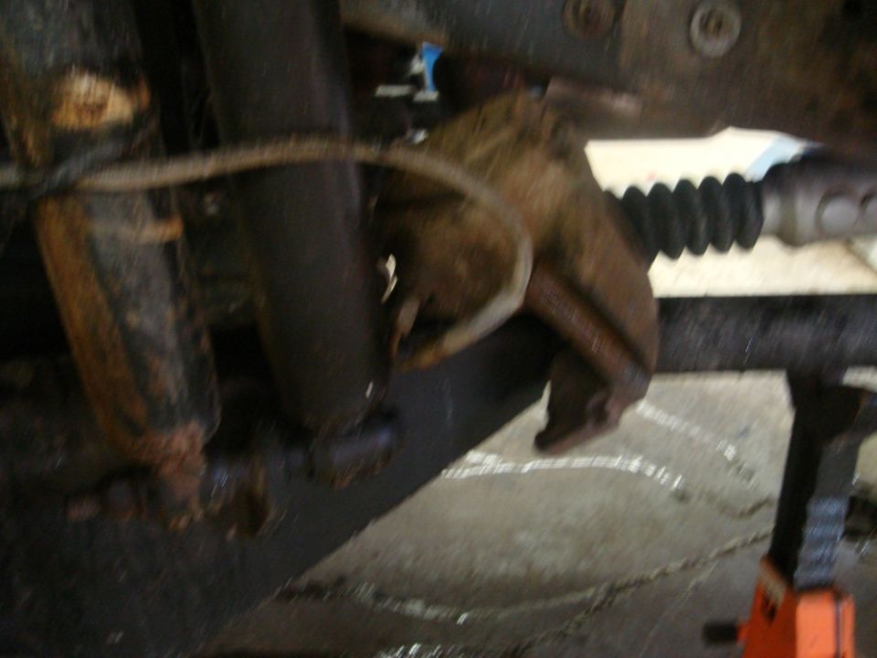 Rusted brake caliper and suspension parts, likely from a truck or SUV