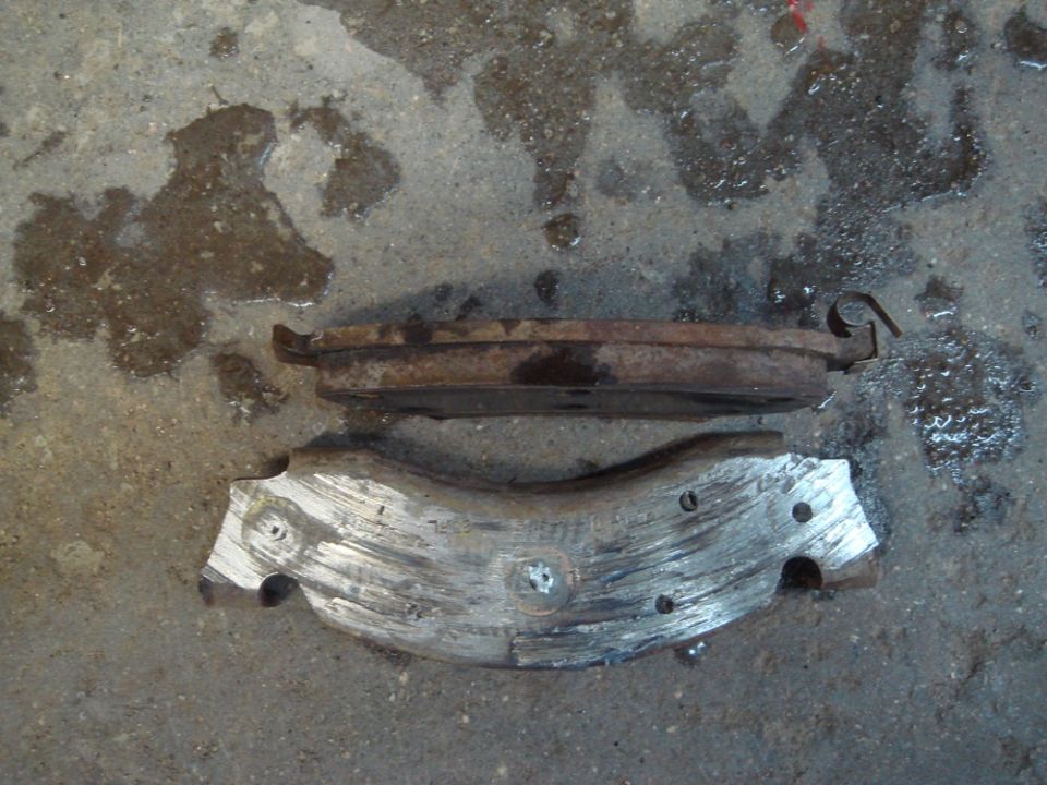 Two worn brake pads on a wet concrete surface. One pad is heavily used and shows metal backing