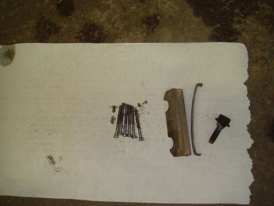 Bunch of brake caliper bolts, a metal bracket, and a spring clip laid out on paper towels