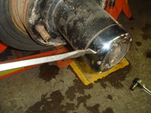 1996 Ford Bronco - Close-up of a vehicle's hub assembly, showing a chrome cap being removed with a pry bar.