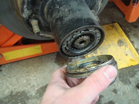 1996 Ford Bronco - A hand holds a removed cap from a vehicle's hub assembly, revealing internal gears and components.