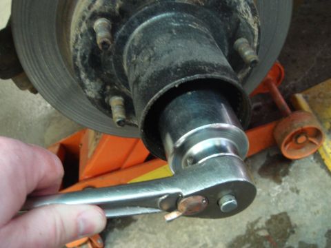 1996 Ford Bronco - A socket wrench is used to work on the wheel hub assembly of a vehicle, which is supported by an orange jack stand.