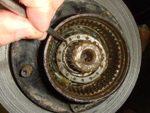 1996 Ford Bronco - A hand uses a tool to pry on a greasy, toothed auto locking hub mechanism.