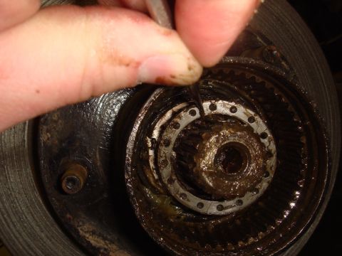 1996 Ford Bronco - A mechanic works on a dirty hub assembly, focusing on a small metal ring within the mechanism.