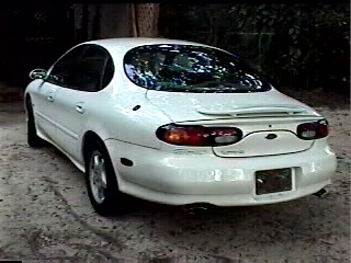 1997 Ford Taurus - A white sedan is parked on a dirt surface, viewed from the rear.