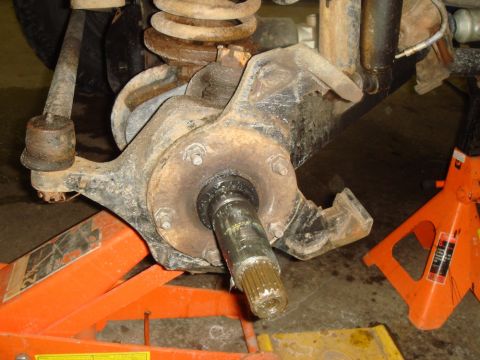 1996 Ford Bronco - Close-up of a vehicle's front wheel hub assembly, showing the splined axle shaft and suspension components, with orange jack stands visible.