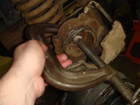 1996 Ford Bronco - Close-up of a hand using a C-clamp on a vehicle's brake caliper and suspension components.