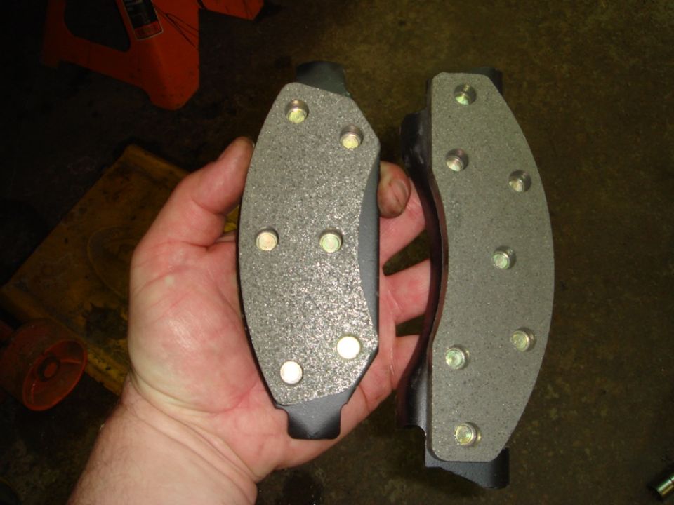 Hand holding two new brake pads with visible hardware
