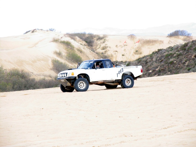 White off-road pickup truck with number 1449 on the side, driving on sand dunes