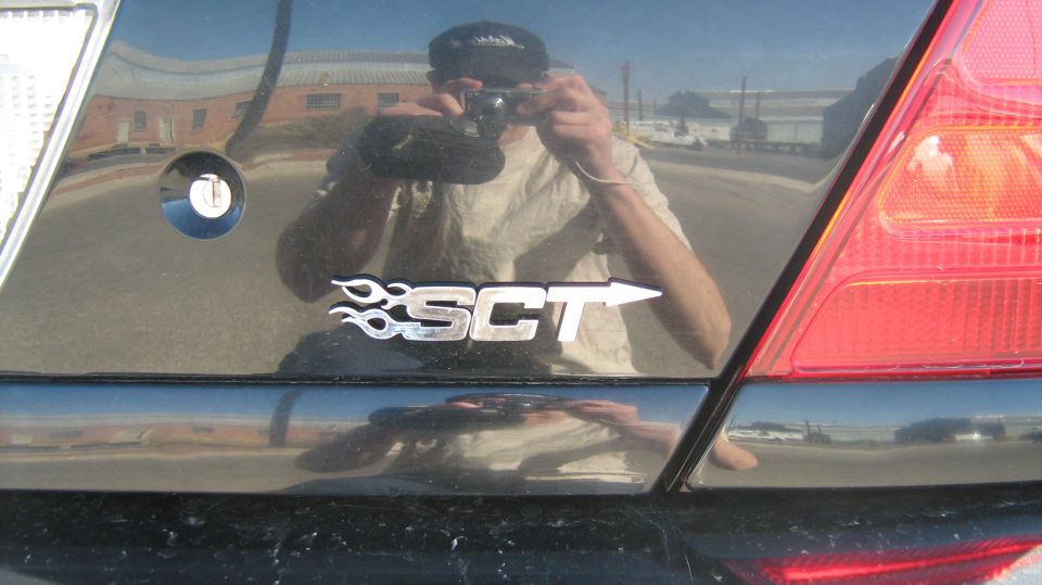 Close-up of a black car's SCT decal with photographer reflected in the paint