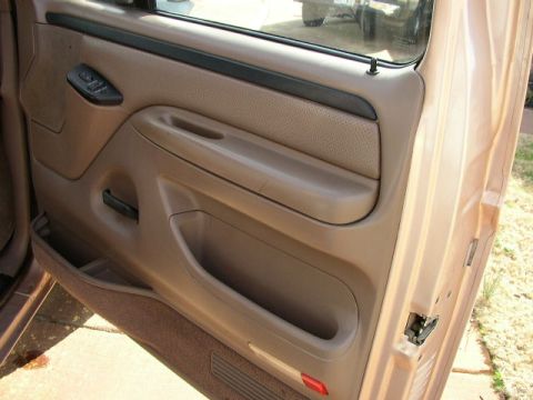 1995 Ford Bronco - The interior door panel of a Ford truck, tan upholstery and a prominent armrest with storage.