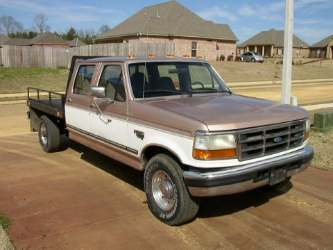 1995 Ford Bronco - This 1995 Ford F-350 flatbed truck is parked on a concrete driveway in front of houses.