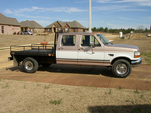 Tan and white Ford F-350 flatbed truck, side view, parked on driveway