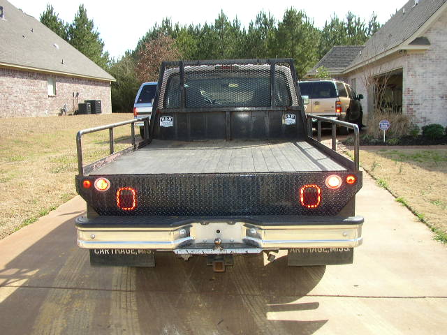 Rear view of a flatbed Ford F-Series truck. Another SUV is parked in the driveway
