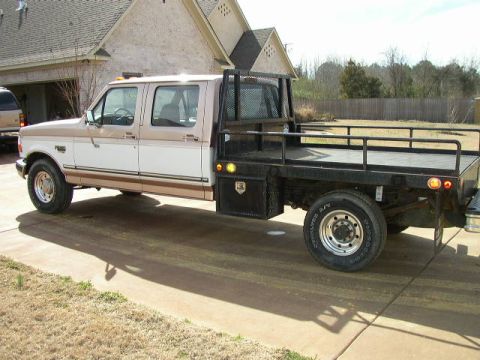 1995 Ford Bronco - This two-tone brown and white crew cab truck features a flatbed with side rails and a toolbox.