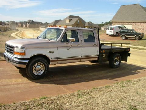 1995 Ford Bronco - This Ford F-350 flatbed truck is parked in front of a suburban house. A van and SUV are visible in the background.