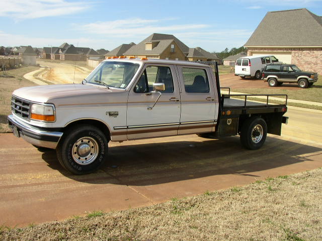 1995 Ford F-350 flatbed truck parked on a driveway, with a white van and black SUV in the background