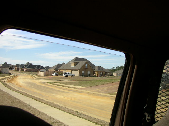 Two white trucks and a white car parked on a dirt road in front of houses