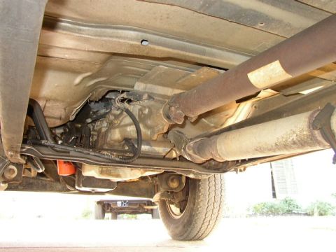 1995 Ford Bronco - Underside view of a vehicle's drivetrain and exhaust system, with another vehicle in the background.