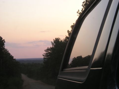 1989 Ford Bronco - View from inside a vehicle looking out at a sunset over a wooded landscape and dirt road.