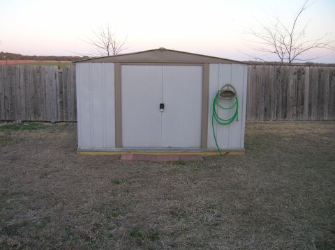 1996 Ford Bronco - A white metal shed with double doors and a green hose hangs on the side, set against a wooden fence.
