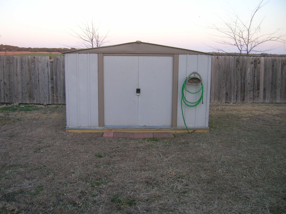 Metal shed with double doors and coiled green hose on wall