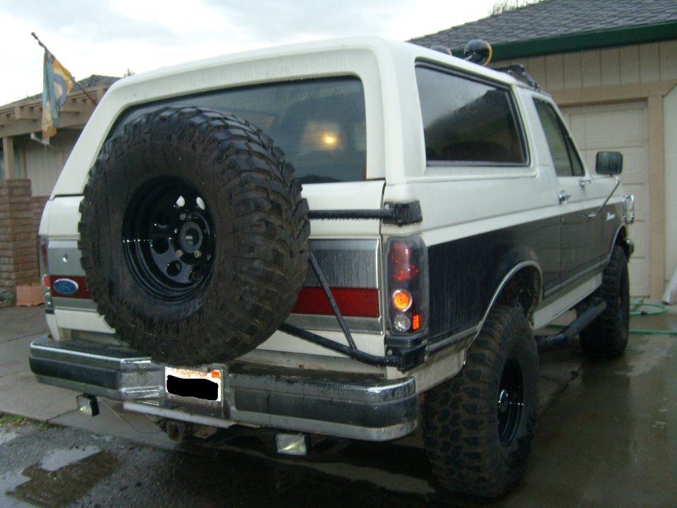 White lifted Ford Bronco from rear with swing-out spare tire carrier and mud tires