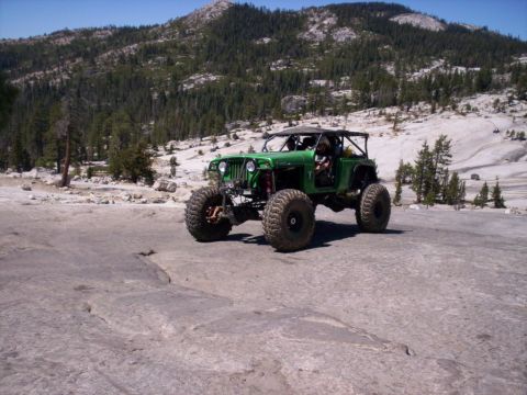 1989 Ford Bronco - A heavily modified green jeep navigates a rocky, off-road trail in a mountainous landscape.