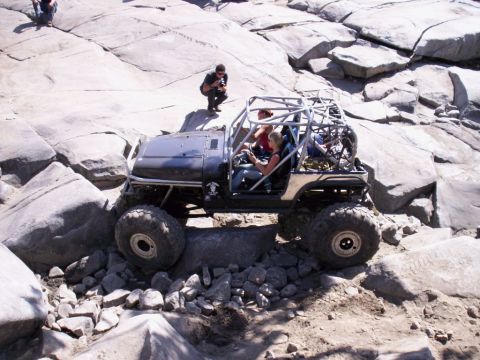 1989 Ford Bronco - A modified off-road vehicle tackles a challenging rocky obstacle course with people inside.