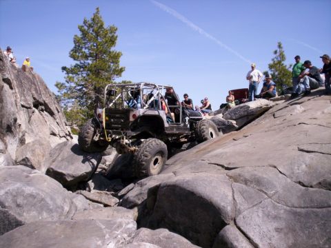 1989 Ford Bronco - Spectators watch an off-road vehicle navigate a rocky trail under a clear blue sky.