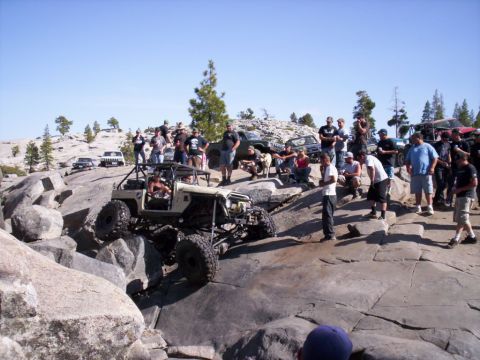 1989 Ford Bronco - A group watches as a custom off-road vehicle tackles a challenging rock formation on a sunny day.