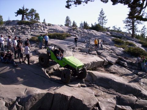 1989 Ford Bronco - A group watches as a custom off-road vehicle tackles a challenging rocky terrain under a clear sky.