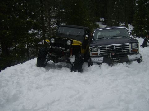 1986 Ford Bronco - Two off-road vehicles, a Ford truck and a Jeep, are partially buried in snow.
