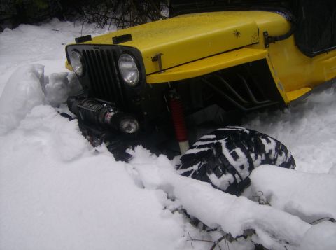 1986 Ford Bronco - Yellow Jeep Wrangler stuck deep in snow, showing front grille and winch.