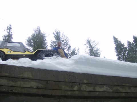1986 Ford Bronco - A man sits in a yellow off-road vehicle partially buried in snow, with trees in the background.
