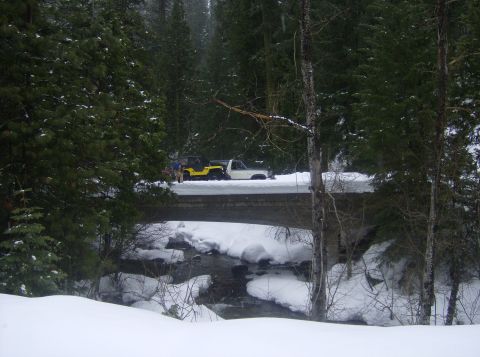1986 Ford Bronco - Two vehicles are stopped on a bridge covered in snow, with a creek flowing below.