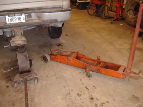 1992 Ford Bronco - A silver 1992 Ford Bronco is lifted on a jack in a garage, with an orange floor jack on the concrete floor.